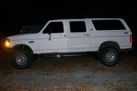 1992 Ford C-350 (Centurion Conversions) - This white extended cab pickup truck has a custom rear body, giving it an SUV-like appearance, and is lifted with 4x4 badging.