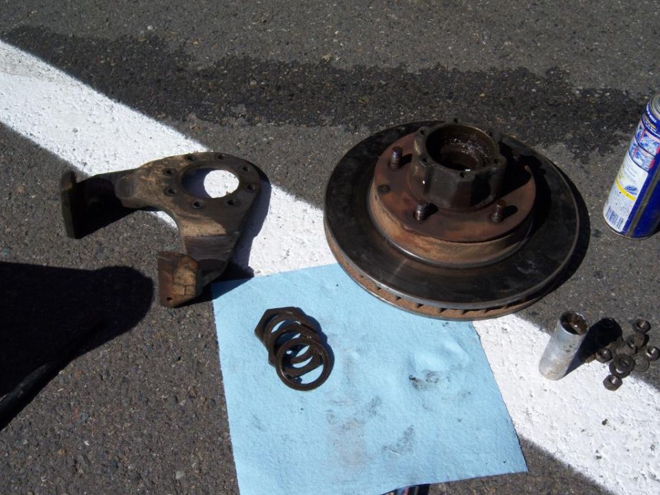 Rusty brake rotor and hub, steering knuckle, nuts and washers on blue towel on asphalt