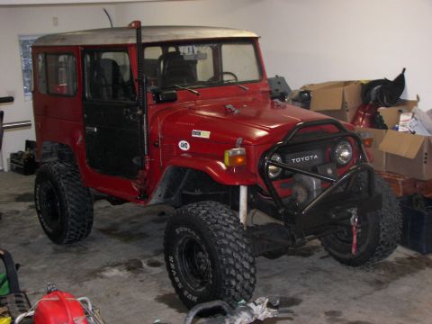 1990 Chevrolet Suburban - A red Toyota Land Cruiser FJ40 is parked indoors with large off-road tires and a custom front bumper.