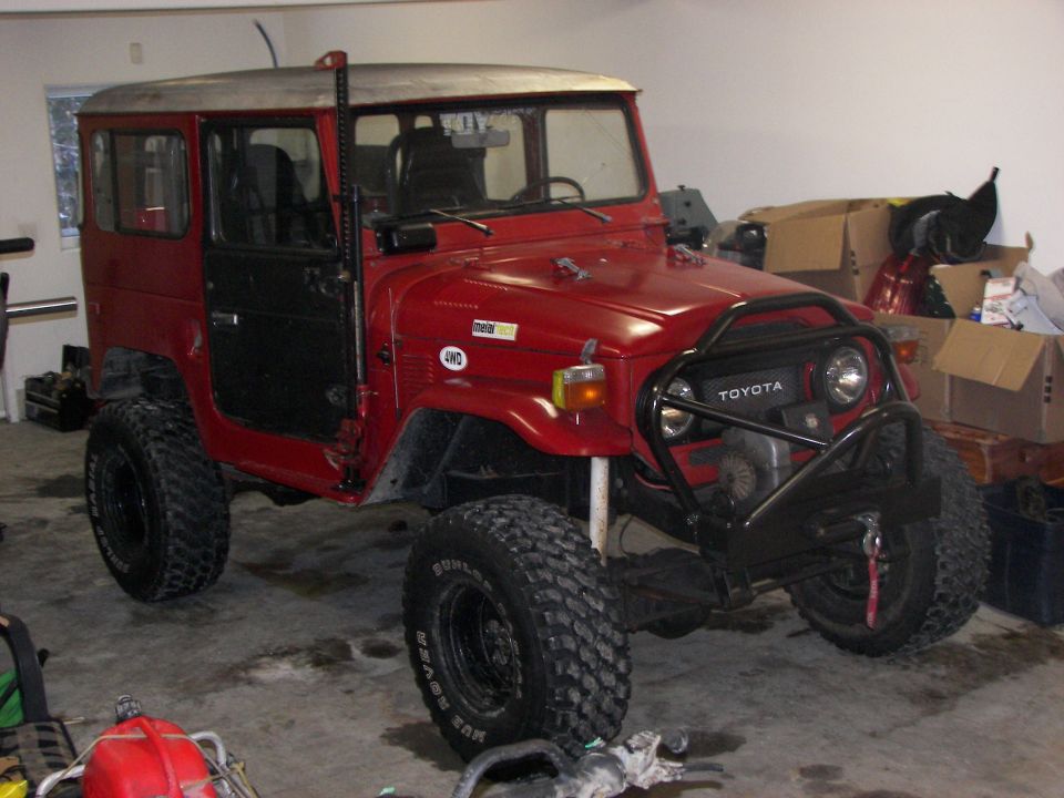 Red Toyota Land Cruiser FJ40 with off-road tires and a brush guard