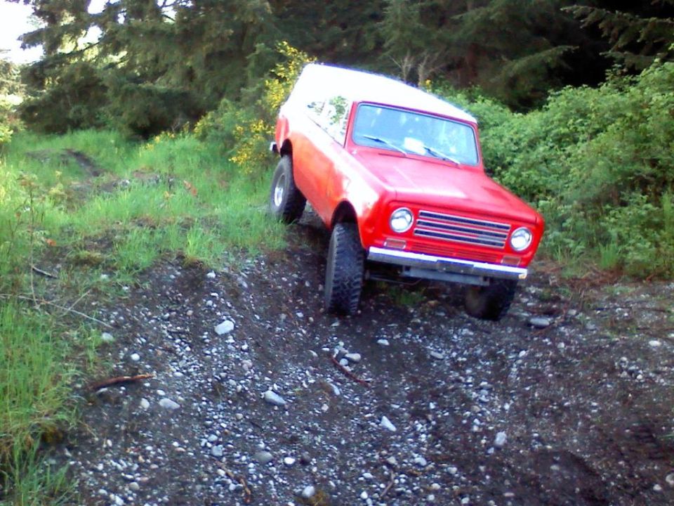 Red 4x4 SUV with white top on knobby tires descending a rocky dirt trail in the woods