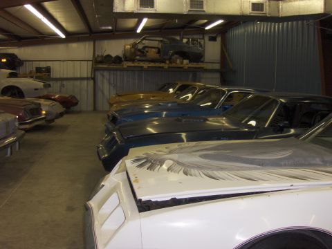 1970 Chevrolet Camaro - A collection of vintage automobiles are stored indoors, with a prominent eagle decal visible on the hood of the closest vehicle.