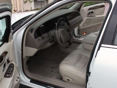2002 Lincoln Town Car - The interior of a car shows tan leather seats, dashboard, and door panels with wood trim accents.