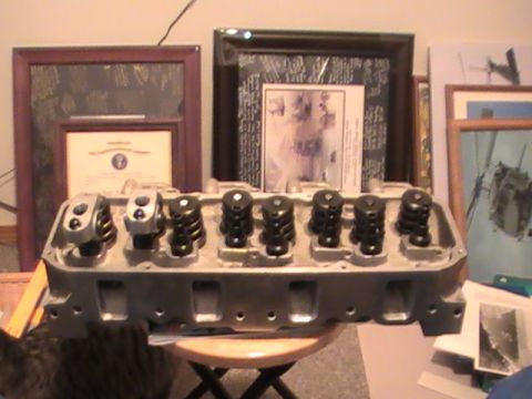 1971 Ford Mustang - Engine cylinder head assembly with valves and springs, displayed indoors with framed items in the background.