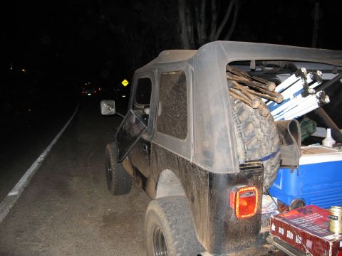 1986 Ford Bronco - A black Jeep Wrangler is parked on the side of a road at night, loaded with camping equipment.