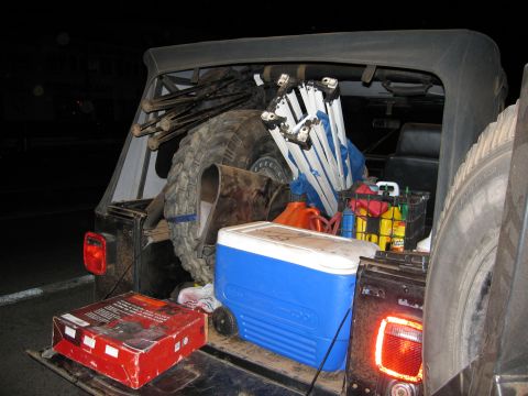 1986 Ford Bronco - Jeep packed with gear for an outdoor trip, including a cooler, spare tire, and gas cans.