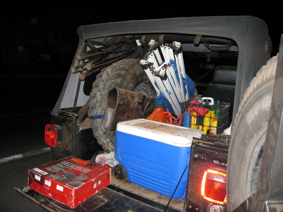 Rear cargo area of a Jeep loaded with a cooler, gas cans, spare tire, and camping equipment