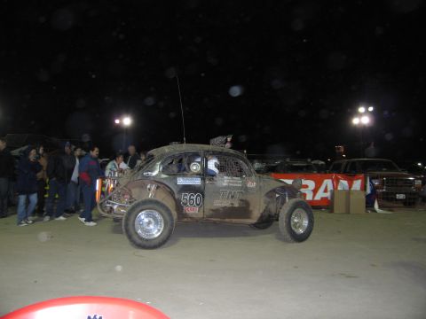 1986 Ford Bronco - A heavily modified Volkswagen Beetle, prepared for off-road racing, sits covered in mud under stadium lights.