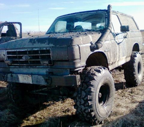 1990 Ford Bronco - This heavily modified SUV, likely from the late 1980s, is covered in mud and equipped for off-road use.