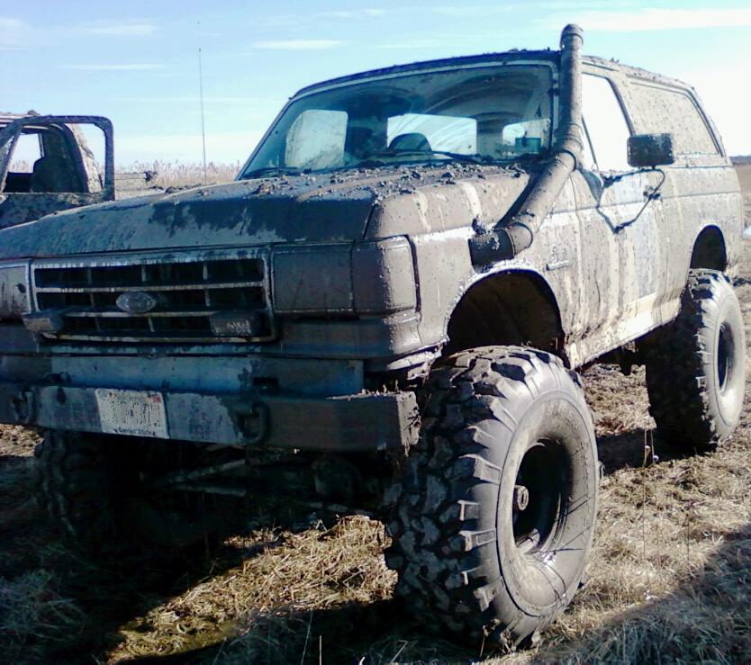 Mud-covered SUV with snorkel, lifted suspension, and large off-road tires. Another vehicle is partially visible to the left