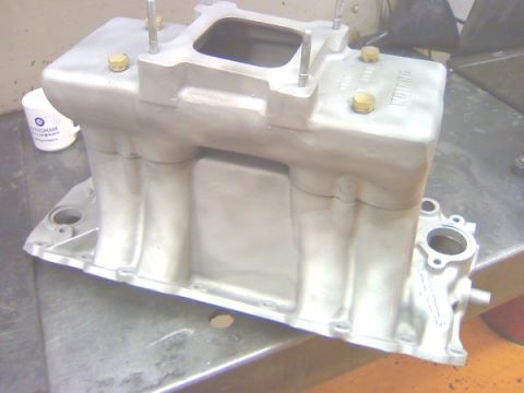 1990 Chevrolet Silverado 1500 - A bare cast-aluminum Weiand tunnel-ram intake manifold sitting on a metal workbench, viewed from the front corner with its tall runners, si…