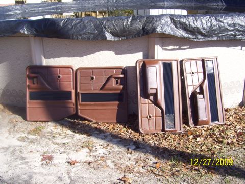 1978 Ford Bronco - Four brown molded door panels leaned in a row against a stucco wall under a black tarp, two flat rear panels on the left and two contoured…