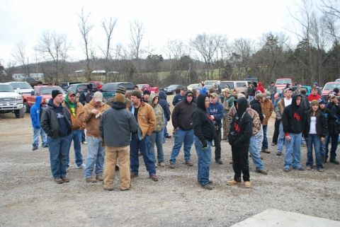 2007 Ford Mustang - A crowd gathers in a gravel lot, surrounded by numerous cars and trucks under an overcast sky.