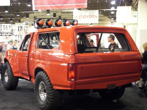 2006 Dodge 2500 - Rear view of an orange Ford Bronco with off-road tires and a roll cage visible inside.