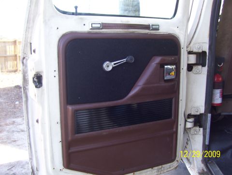 1978 Ford Bronco - Interior view of a vehicle door panel, showing brown and black trim with a chrome window crank. A fire extinguisher is also visible.