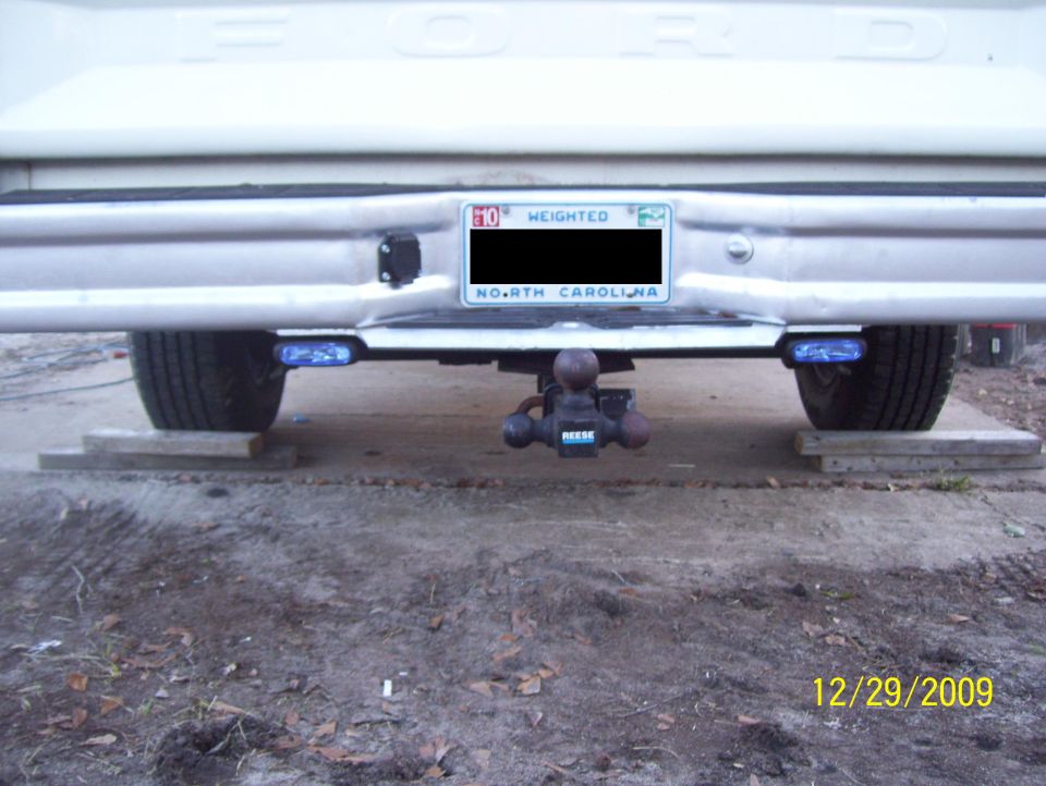 Rear bumper of a pickup truck with a Reese hitch and blue trailer lights. North Carolina license plate visible