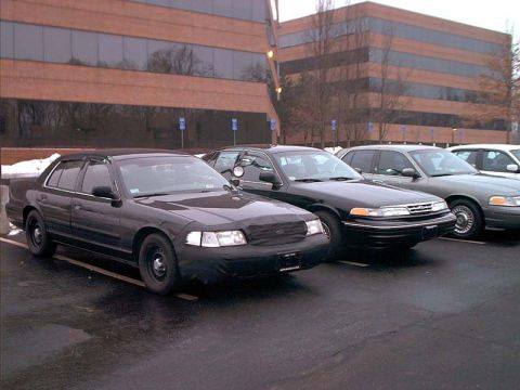 2000 Ford Crown Victoria - Several police cars are parked in a lot in front of an office building.