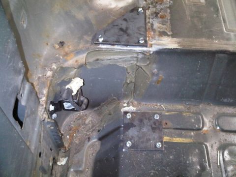 1996 Ford Bronco - Metal plates are bolted to the rusted interior floor of a vehicle, likely for a roll cage.
