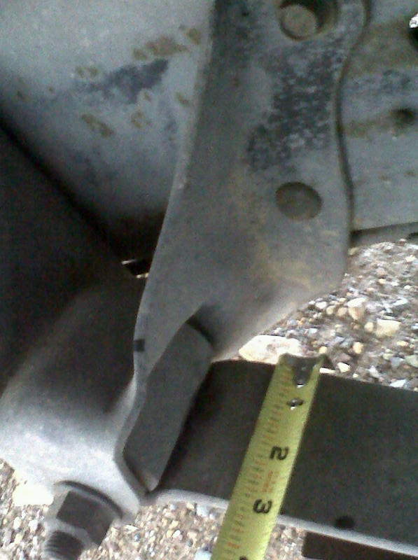 Close-up of a metal bracket and bolt on a vehicle frame, with a yellow tape measure showing 2 inches
