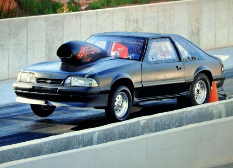 1990 Ford Mustang - A 1990 Ford Mustang drag car with a dragon decal on its hood scoop is captured in motion on a race track.