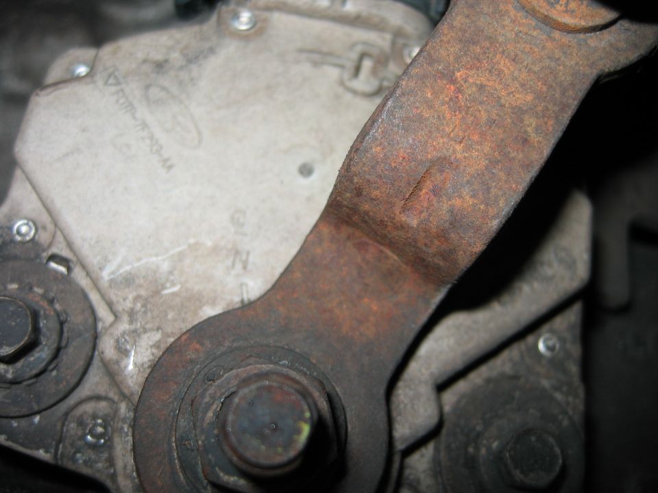 Rusty steel bracket bolted to a cast aluminum housing with a large hex bolt.
