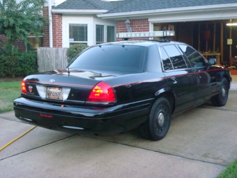 2003 Ford Crown Victoria - A black sedan, possibly a police vehicle, is parked in a driveway with a light bar mounted on its roof.