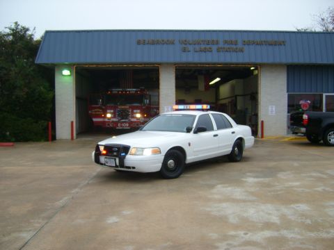 2003 Ford Crown Victoria - A white police car is parked outside the Seabrook Volunteer Fire Department's El Lago Station, with a fire truck visible inside.