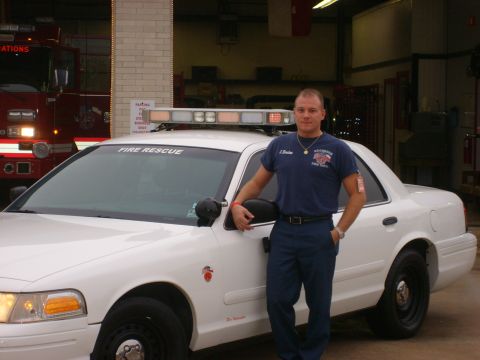 2003 Ford Crown Victoria - A firefighter poses next to a white vehicle marked 'FIRE RESCUE' inside a fire station.