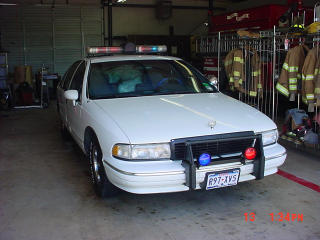 White police car with light bar and push bumper parked inside a garage