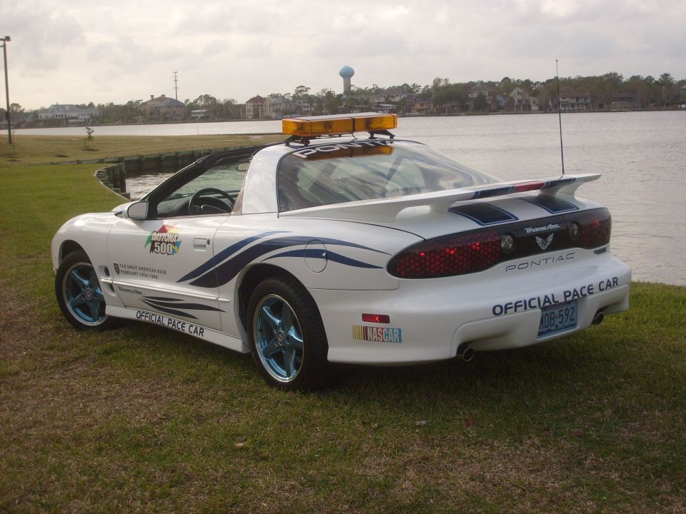 White Pontiac Firebird with blue racing stripes and 'Official Pace Car' decals, parked on grass near water