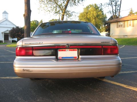 1995 Mercury Grand Marquis - The rear of a 1995 Mercury Grand Marquis is shown parked in a lot with a church and house in the background.