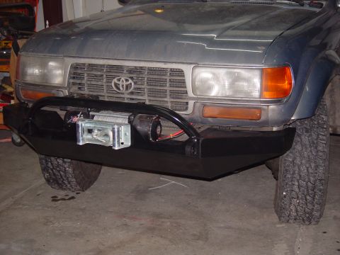 1993 Ford Bronco - The front of a dark-colored Toyota Land Cruiser is shown, a custom black bumper with a winch.