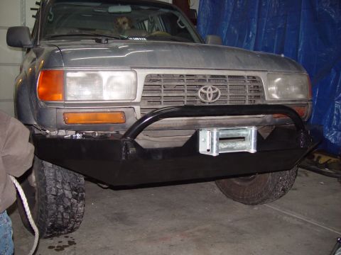 1993 Ford Bronco - Grey Toyota Land Cruiser with a custom bumper and winch installed. The vehicle's front end is visible, including the grille and headlights.