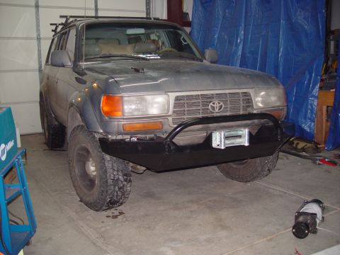 1993 Ford Bronco - Toyota Land Cruiser with aftermarket bumper and winch, parked indoors.