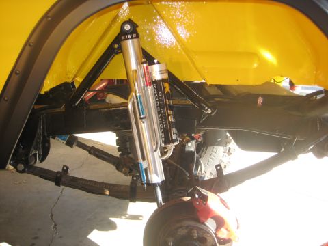 1970 Ford Bronco - Close-up of a yellow vehicle's suspension system, highlighting the shock absorbers and leaf springs.