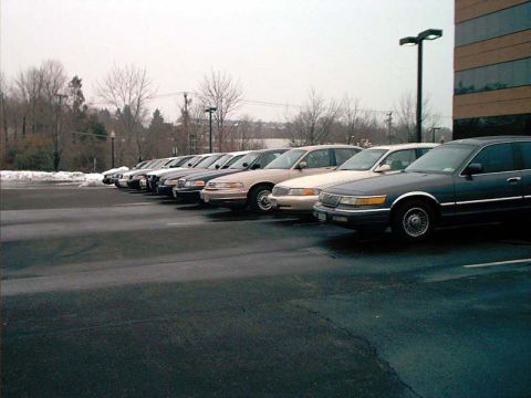 2000 Ford Crown Victoria - A row of sedans are parked in an outdoor lot under an overcast sky.