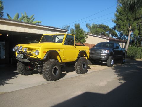 1970 Ford Bronco - Modified 1970 Ford Bronco and a pickup truck are parked outside a garage on a sunny day.