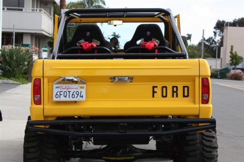 1970 Ford Bronco - Rear view of a yellow Ford Bronco, modified with racing seats and a roll cage, displaying "FORD" lettering.