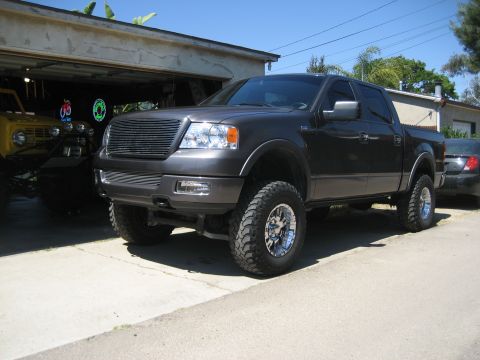 2005 Ford F-150 - Lifted Ford F-150 pickup truck with aftermarket wheels parked outside a garage.