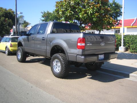 2005 Ford F-150 - A lifted gray Ford F-150 pickup truck is parked on the street next to a yellow Mini Cooper.