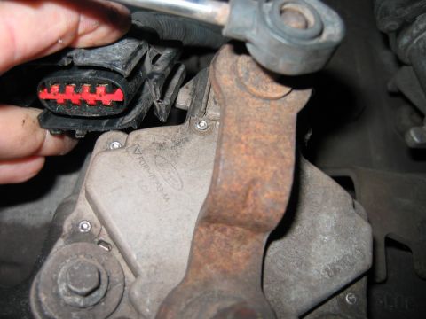 1992 Ford Bronco - Close-up of a dirty Ford component with a cast part marked 'F0TU' and the Ford logo, alongside a fingers holding a black electrical connect…