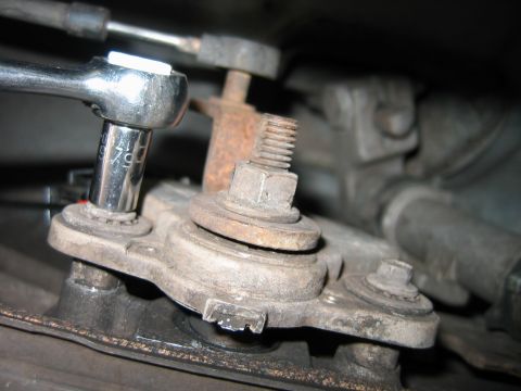 1992 Ford Bronco - Close-up of a rusty hex bolt with exposed threads on a metal mounting bracket, being loosened by a chrome socket wrench with a 3/8-inch dri…