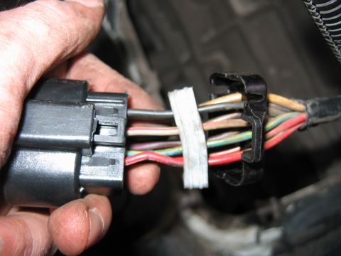 1992 Ford Bronco - A hand holds a disconnected black multi-pin electrical connector with numerous colored wires (red, green, tan, gray) exiting from it, wrapp…
