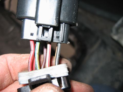 1992 Ford Bronco - Close-up of a hand holding two black plastic electrical connectors with multiple colored wires (red, green/yellow, pink/white, gray, tan) e…