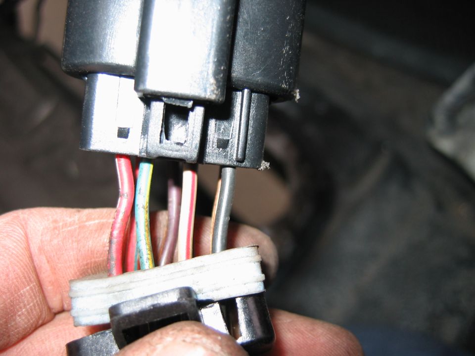 Hand holding disconnected black automotive electrical connectors with colored wires