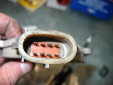 1992 Ford Bronco - Close-up of an electrical connector held in a person's fingers, showing an oval housing with a corroded orange terminal block and multiple…