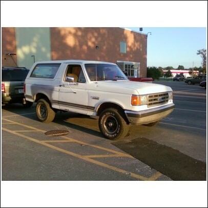 1989 Ford Bronco - A white 1989 Ford Bronco is parked in a lot with a building in the background.
