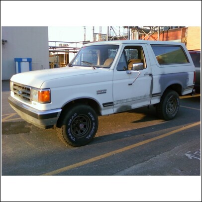 1989 Ford Bronco - A white 1989 Ford Bronco is seen from a 3/4 front angle in a parking lot.