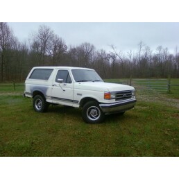 1989 Ford Bronco - This white Ford Bronco is parked outside on a cloudy day with trees in the background.