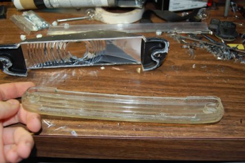 1985 Mercury Grand Marquis - A disassembled car headlight assembly and its clear lens are shown on a workbench.